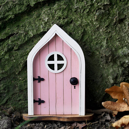 Miniature pink fairy garden door set within an enchanted tree, featuring a small window, surrounded by lush greenery and resembling a whimsical cottage with birdhouse accents.