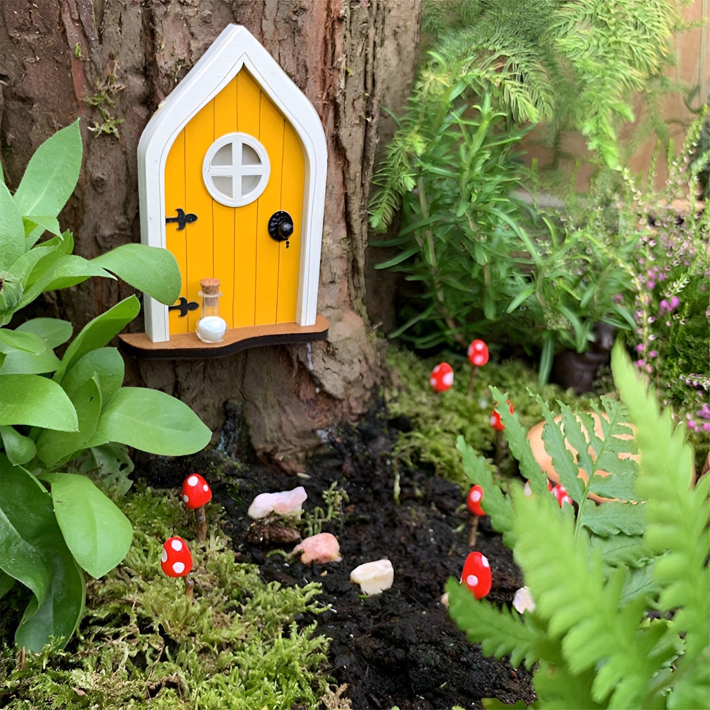 Miniature fairy garden door nestled against a tree, surrounded by lush green foliage and small colorful flowers, creating an enchanting woodland scene.