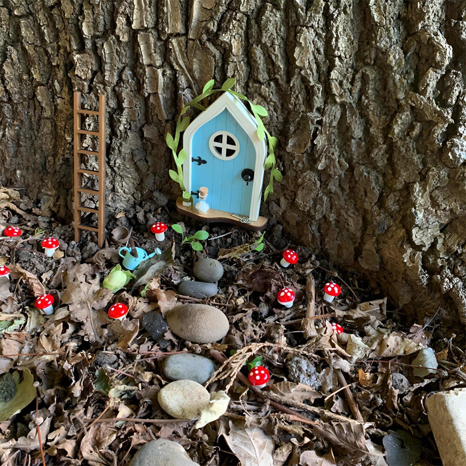Miniature fairy garden door set against a tree trunk surrounded by branches, twigs, and leaves, creating an enchanting woodland atmosphere.