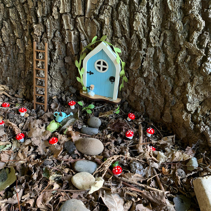 Miniature fairy garden door set against a tree trunk surrounded by branches, twigs, and leaves, creating an enchanting woodland atmosphere.